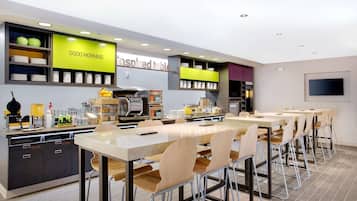 Um restaurante moderno com um balcão extenso, várias áreas de estar e cozinha visível ao fundo.