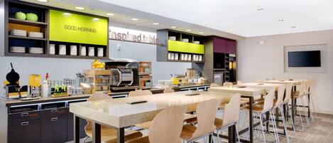 Un restaurante moderno con una barra larga, varias zonas de estar y una cocina a la vista.