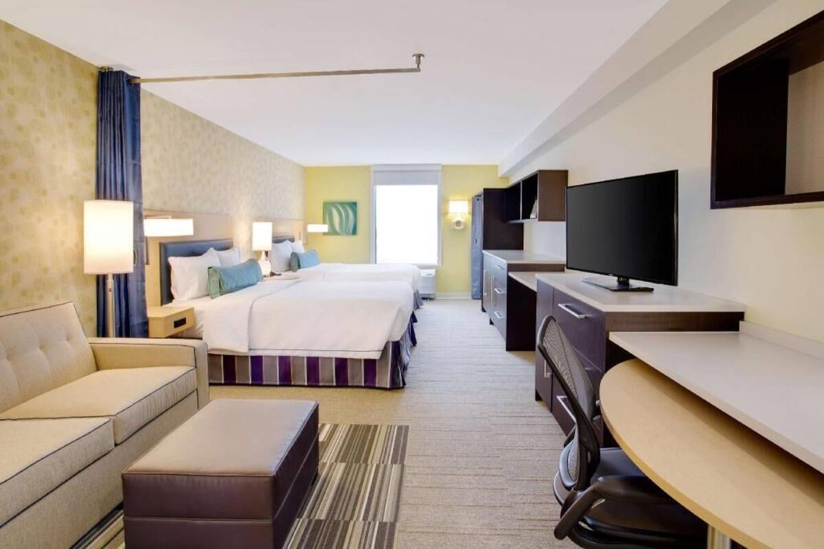 Ein Hotelzimmer mit Bett, Sofa, Schreibtisch, Fernseher und Fenster.