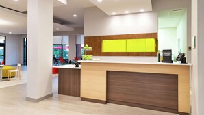 A modern hotel reception area with a wooden reception desk, a bright yellow accent wall, and a visible Hilton sign. - Home2 Suites by Hilton Columbia Downtown (Columbia)