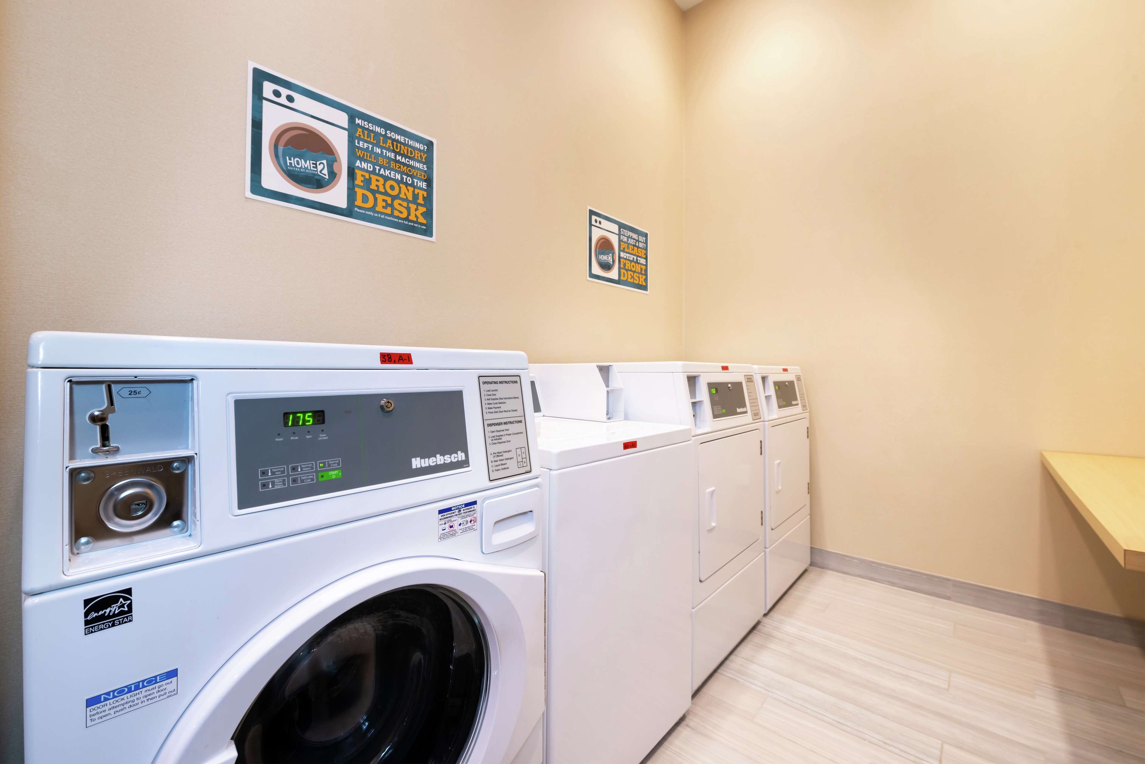 A laundry room with multiple washing machines and dryers, a wooden floor, and two signs on the wall.