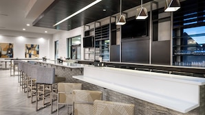 A modern bar area with a long counter, multiple seating options, and a large window offering a view. - Home2 Suites by Hilton Columbia Downtown (Columbia)