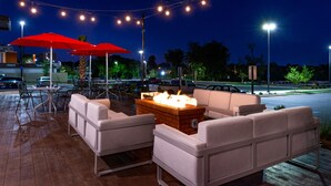 An outdoor seating area with white sofas, red umbrellas, and a fire feature. - Home2 Suites by Hilton Columbia Downtown (Columbia)