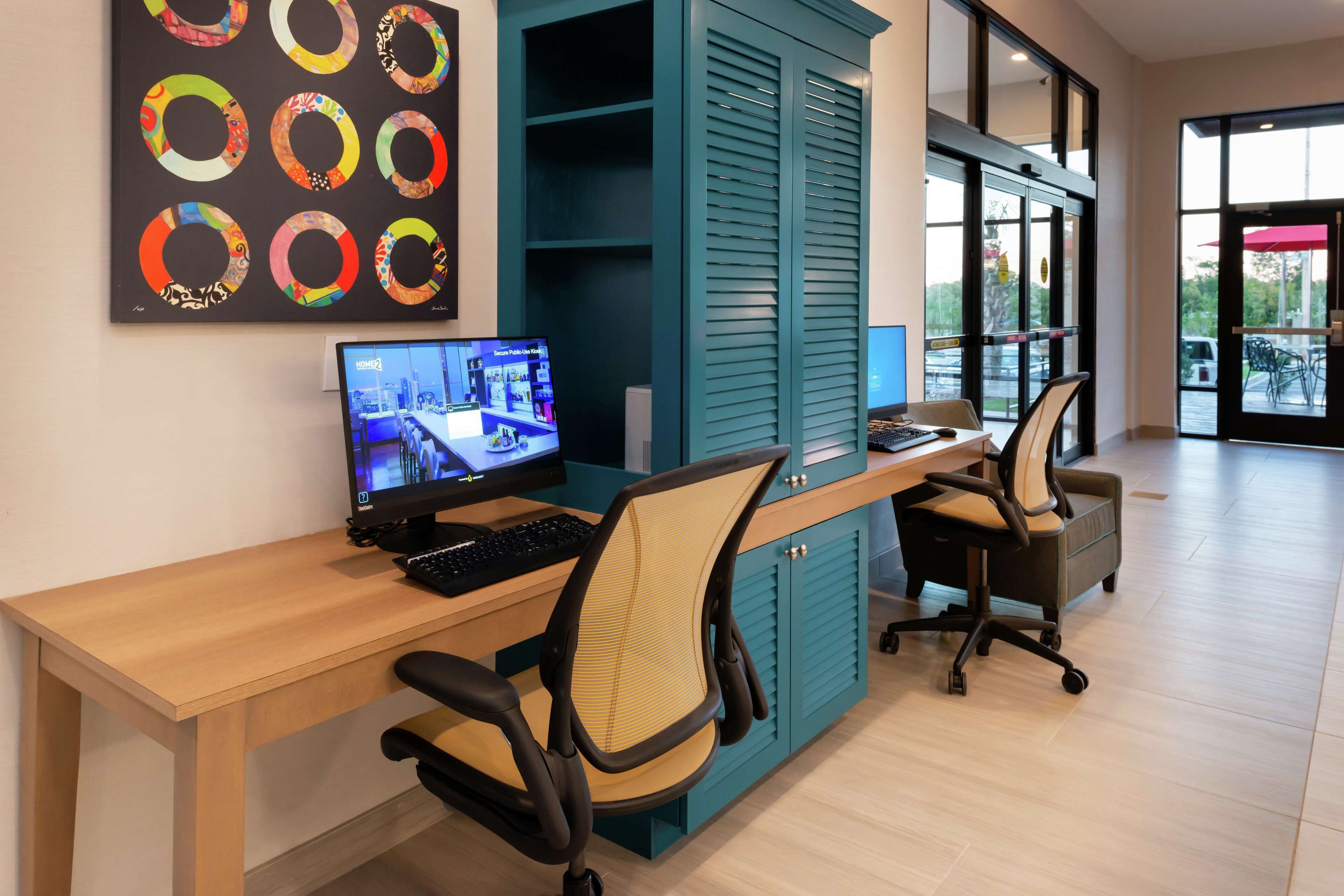 A modern office space with a wooden desk, two office chairs, a computer, and teal cabinets.