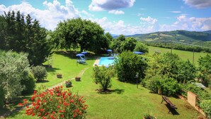 Zona de piscina con sombrillas azules, rodeada de abundante vegetación y árboles.