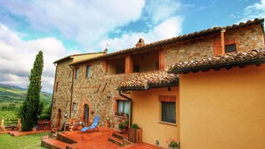 Un edificio de piedra con tejado de tejas, balcón y patio con una silla y una mesa.