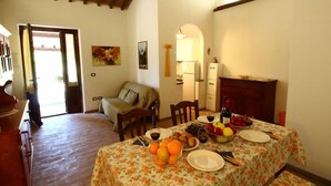 Un coin repas avec une table dressée pour deux personnes, agrémenté d’une nappe à motifs floraux, d’assiettes, de couverts et d’un saladier rempli de fruits.