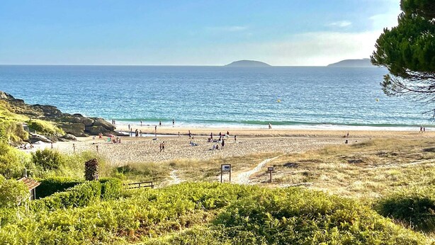 Una playa con gente, cielo despejado y una isla distante.