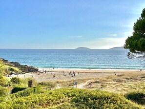 Una playa con gente, cielo despejado y una isla distante.