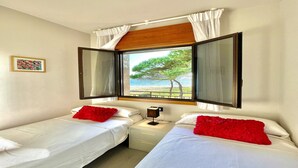 Una habitación con dos camas, una ventana con cortinas, una mesita de noche y una pequeña mesa.