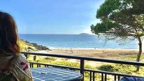 Un balcón con mesa y sillas que da a una playa con un árbol y una isla distante.