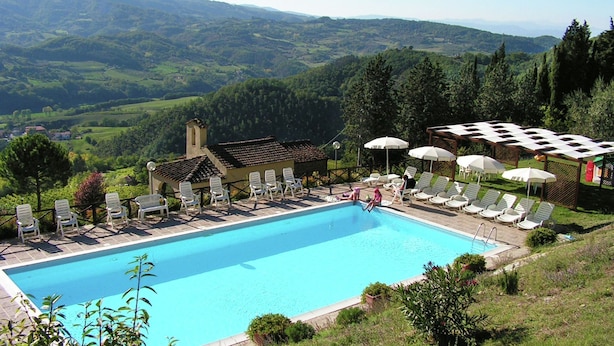 Une piscine entourée de chaises longues et de parasols, bordée d’une végétation luxuriante et offrant une vue sur un paysage montagneux.
