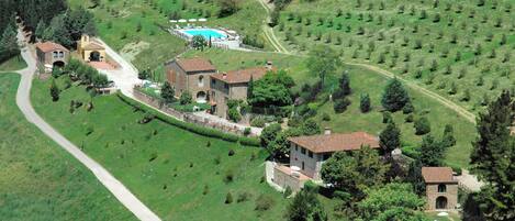 An aerial view of a rural estate with multiple buildings, a swimming pool, and terraced fields.