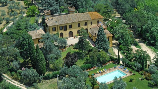 Une grande villa jaune dotée d’une piscine, le tout entouré d’une végétation luxuriante.