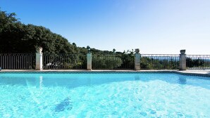 Une piscine d’un bleu éclatant, entourée d’une clôture en métal et de colonnes, et bordée de verdure.