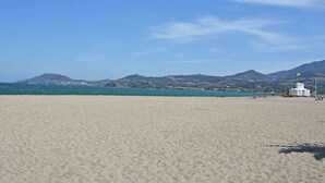 Une plage avec un bâtiment blanc, un ciel bleu clair et des collines à l’horizon.