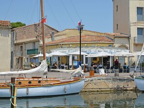 Un restaurant situé au bord de l’eau, avec une terrasse et un voilier amarré à proximité.