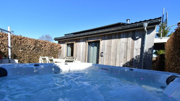 Een hottub voor een houten gebouw met een deur en ramen.