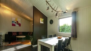 Een moderne eetruimte met een witte tafel en stoelen, een donker houten vloer, een bank met kussens, een vaas en een tak met decoratieve objecten.