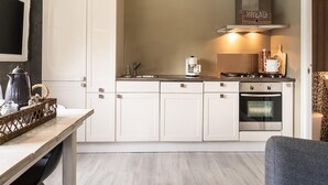 Una cuina moderna amb armaris blancs, fogó a gas, cafetera i cistella penjada.