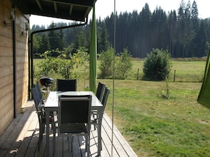 An outdoor wooden deck with a table and chairs, overlooking a grassy field and a forested area. - Family Escape with Garden (Turquestein Blancrupt)