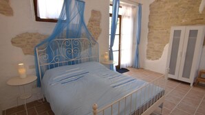 A bedroom with a bed, a nightstand, a window with curtains, a wardrobe, and a stone wall. - Cozy Couples Getaway w/ wifi (Pergola)