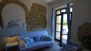 A room with a stone wall, a blue sofa, a small table with a lamp, and a view through a glass door. - Cozy Couples Getaway w/ wifi (Pergola)