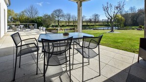 A covered patio with a table and chairs, overlooking a landscaped garden and a lake. - Peaceful Garden Retreat, Epiniac (Epiniac)
