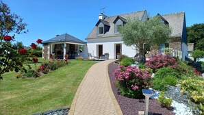 A two-story house with a covered patio, a garden with colorful flowers, and a paved walkway. - Peaceful Garden Retreat, Epiniac (Epiniac)