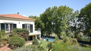 A two-story house with a swimming pool, surrounded by lush greenery and trees.