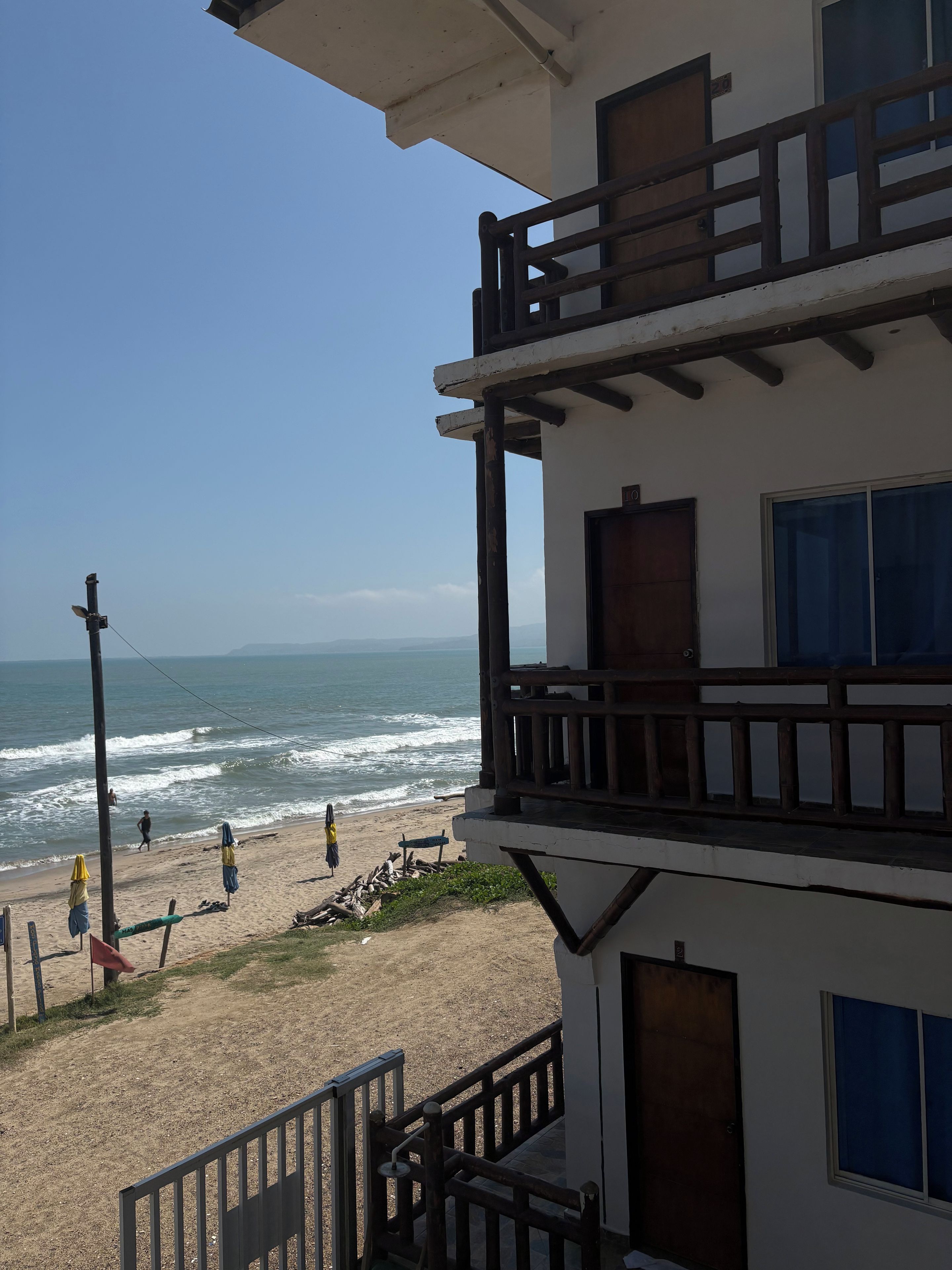 Un edificio con balcón que da a una playa con olas y gente.