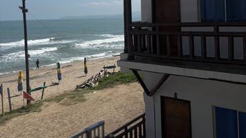 Un edificio con balcón que da a una playa con olas y gente.