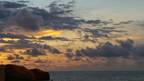 Un atardecer costero con nubes y la silueta de una formación rocosa.