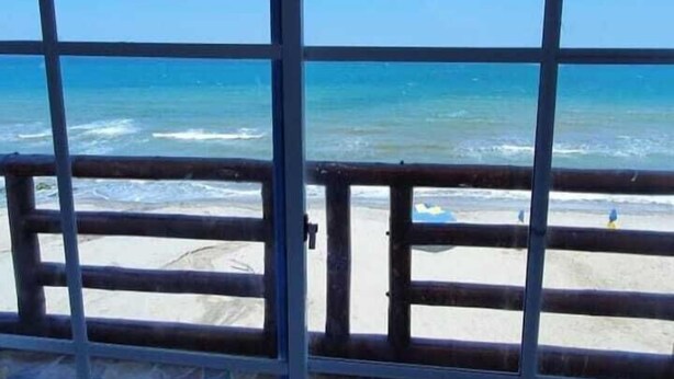 Vista de playa a través de una ventana con celosía metálica, arena y océano.