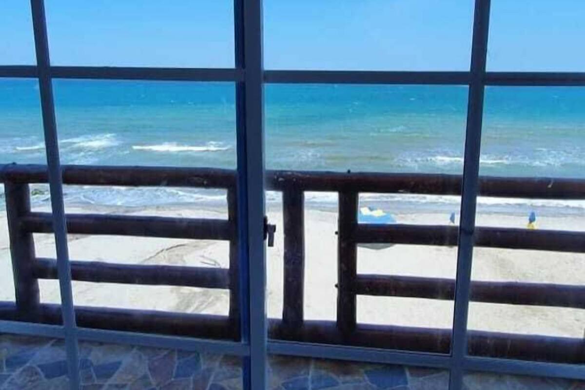 A beach view through a window with a metal grid, sandy beach, and ocean.