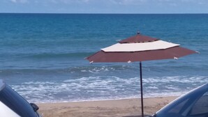 Una sombrilla de playa con parte superior blanca y parte inferior marrón, ubicada en una playa arenosa con el océano al fondo.