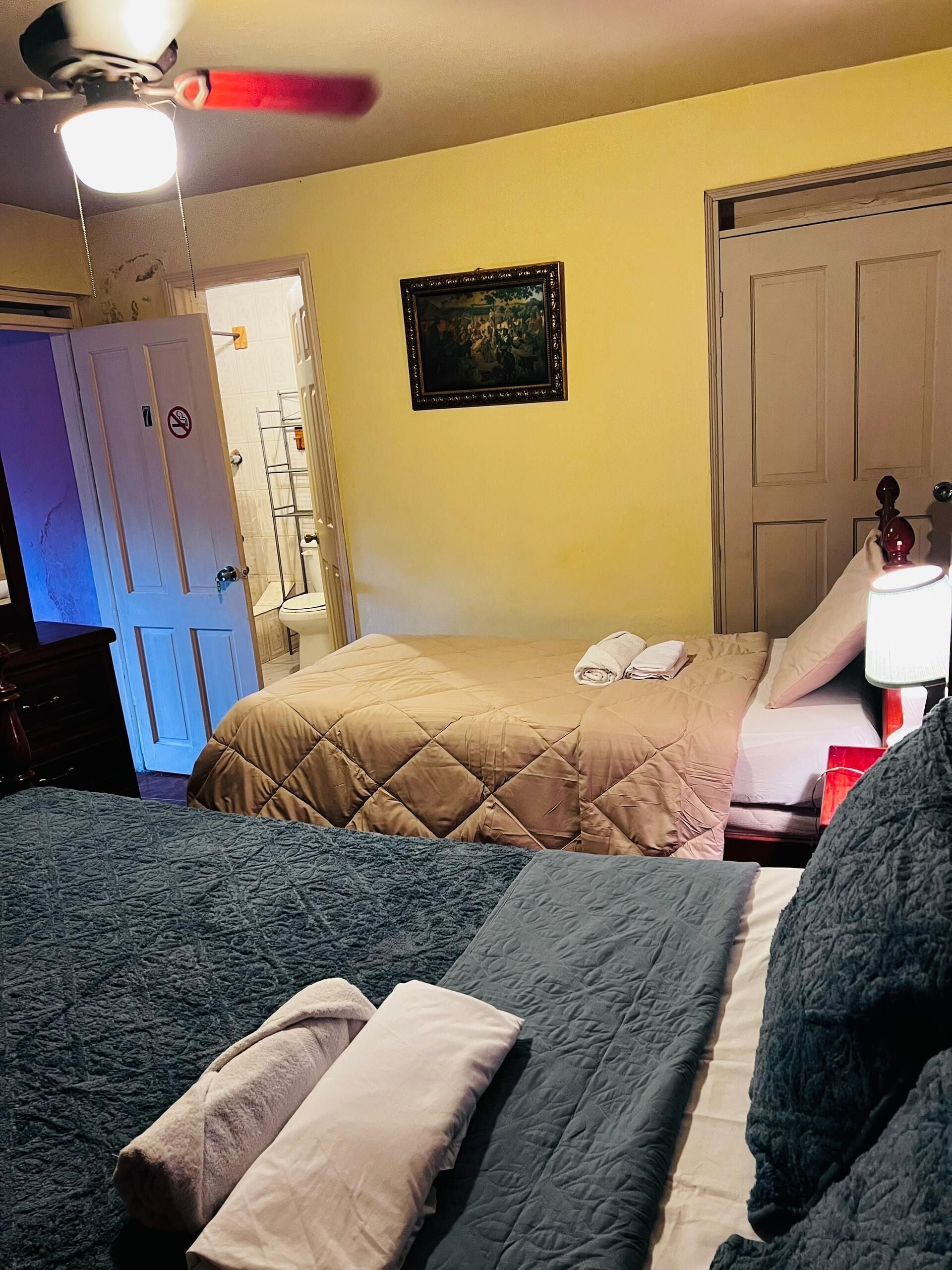 A bedroom with two beds, a ceiling fan, a door with a no-smoking sign, and a framed picture on the wall.