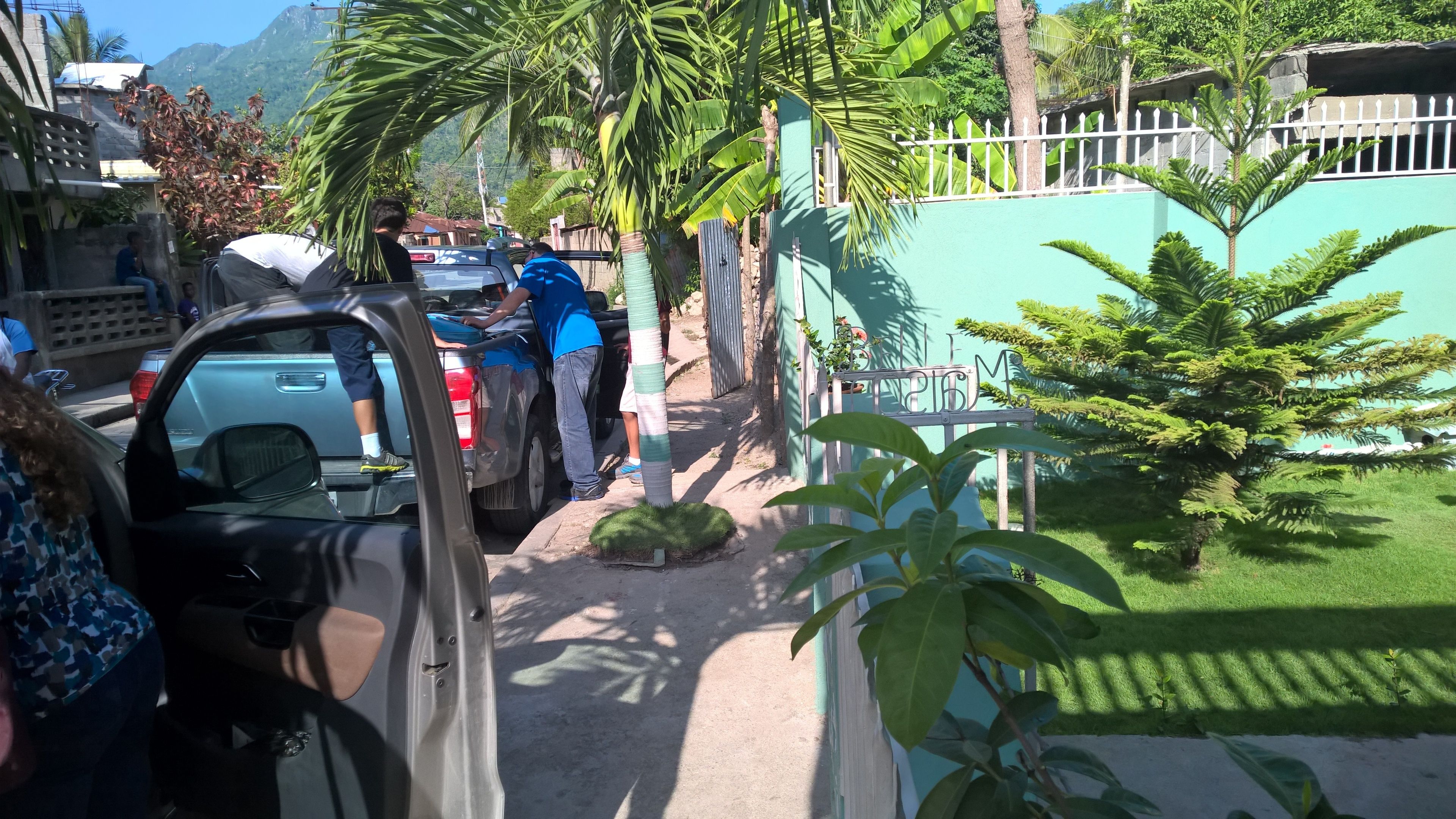 Rua estreita com carros estacionados e pessoas perto de um edifício.