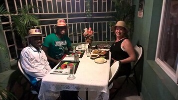 Una mesa de comedor con mantel de encaje, rodeada de sillas, en una habitación con paredes verdes y un ventanal.