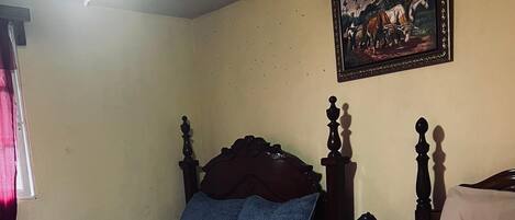 Habitación de hotel con dos camas, una con colcha azul y la otra con colcha color beige. Hay un cuadro en la pared y un ventilador de techo sobre las camas.