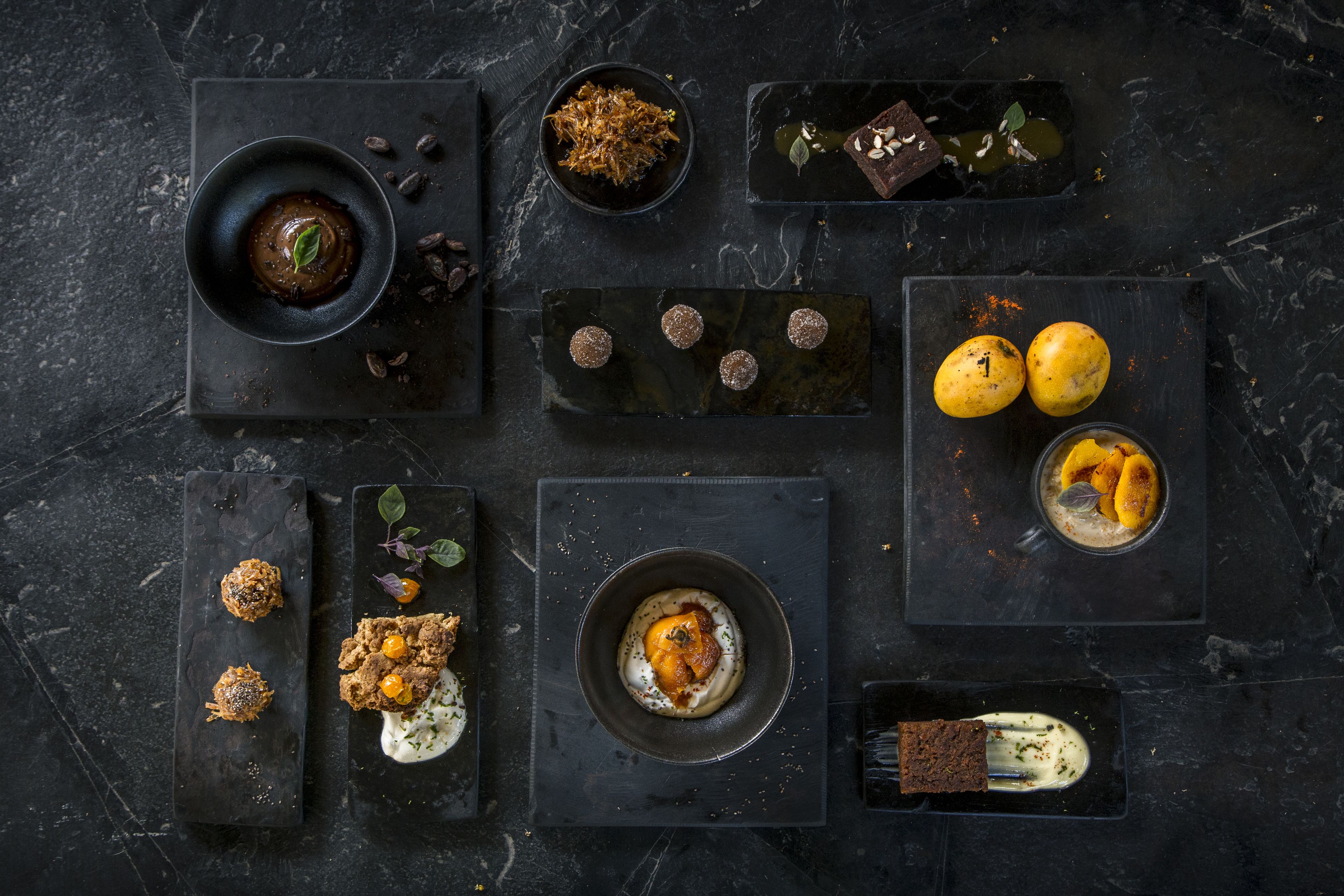 Variedad de postres y bebidas dispuestas sobre bandejas de pizarra oscura.
