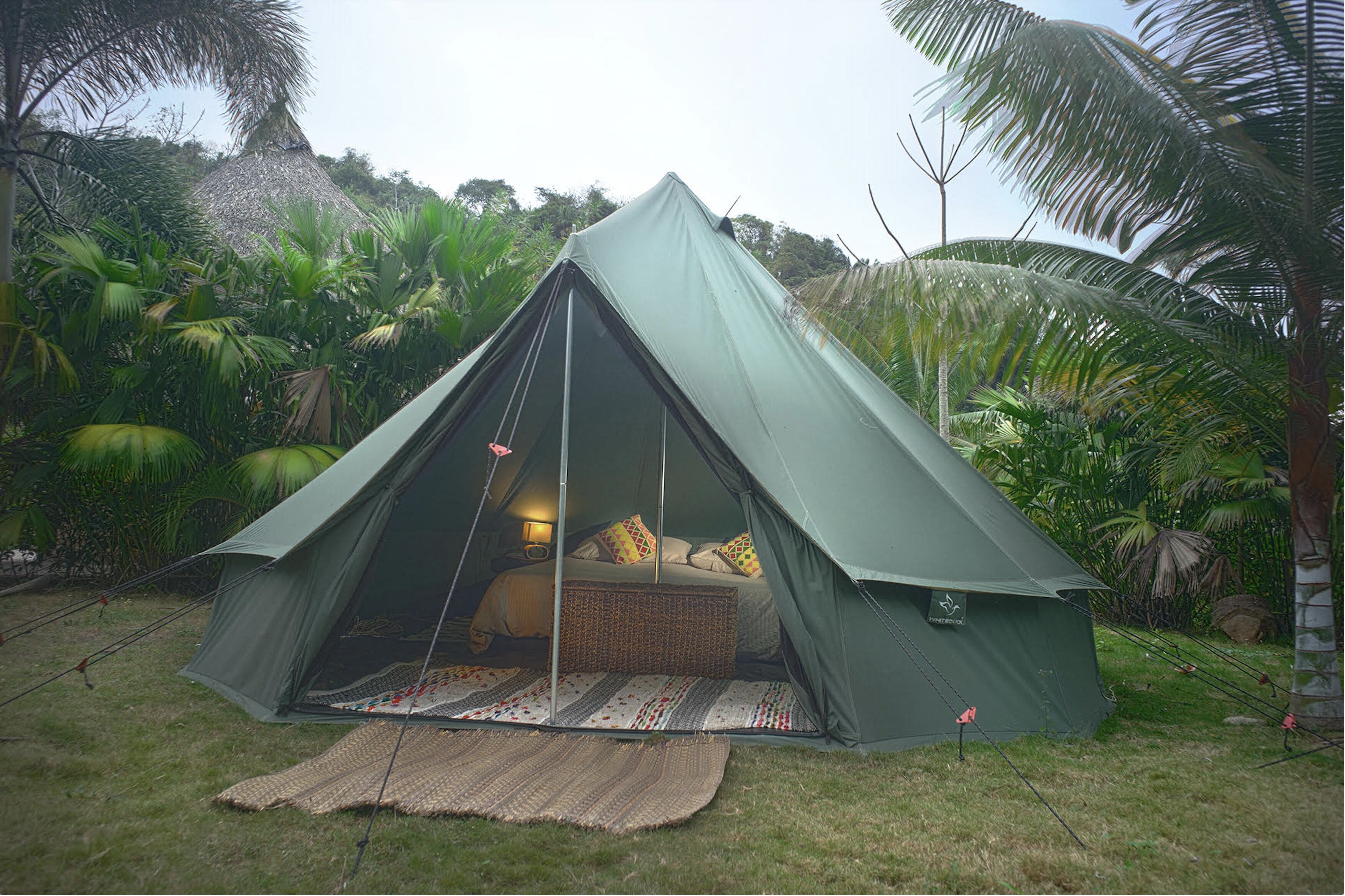 Ein grünes Zelt mit einem Bett im Inneren, umgeben von üppiger Vegetation.