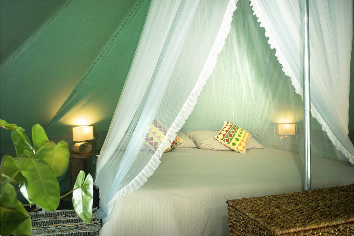 Una camera da letto con tenda e un letto a baldacchino, due lampade ai comodini e una panca in vimini.