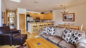 A spacious living area with a sofa, coffee table, and a kitchen with wooden cabinets and a bar. - Pines 101 Ski in out 4 BR Town House (Breckenridge)