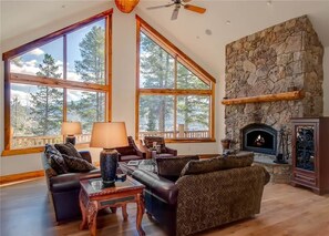 A spacious living room with large windows, a stone fireplace, and a ceiling fan. - A Lookout Lodge House (Breckenridge)