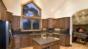 Une cuisine dotée de meubles en bois, de plans de travail en granit, d’une grande fenêtre et d’une cheminée en pierre.