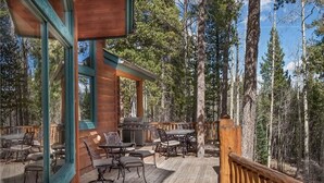 Une terrasse en bois, dotée de mobilier d’extérieur, d’un barbecue et offrant une vue sur une forêt.
