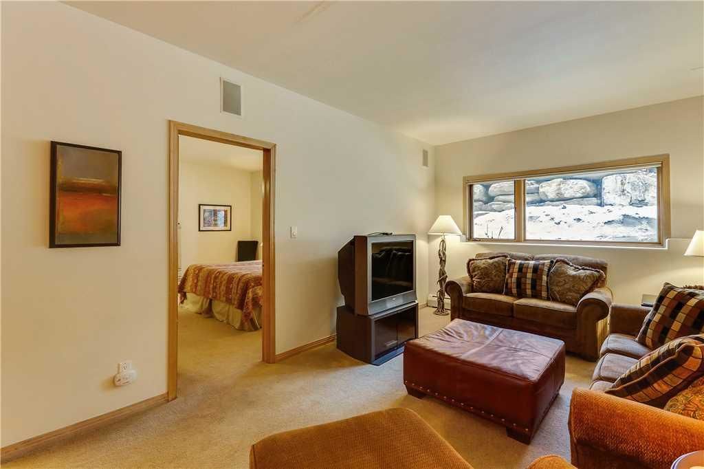 A living room with a sofa, ottoman, and a TV stand. There is a window with a view of a snowy landscape.