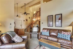 A spacious living room with a brown leather sofa, a wooden coffee table, and a staircase leading to an upper level.