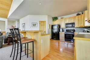A modern kitchen with wooden cabinets, a central island, a refrigerator, and a stove. - Windward Way Retreat House (Steamboat Springs)